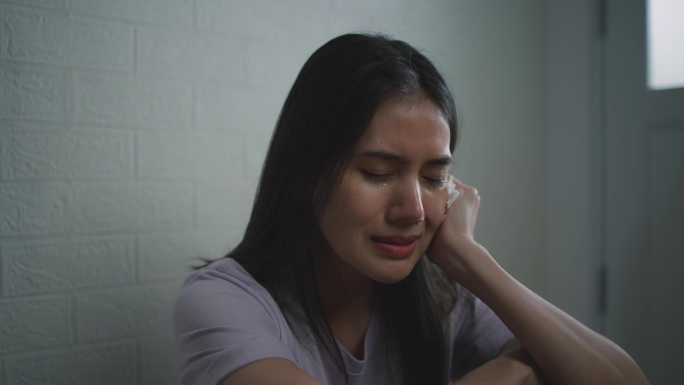 悲伤沮丧的年轻亚洲女子独自坐在客厅地板上哭泣
