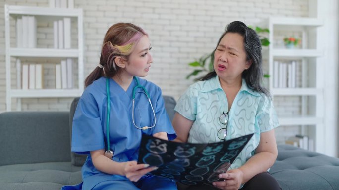 年轻的亚洲女医生向老年病人展示x光扫描，向诊所的妇女解释筛查胶片。老年妇女看完x光片后担心健康检查结