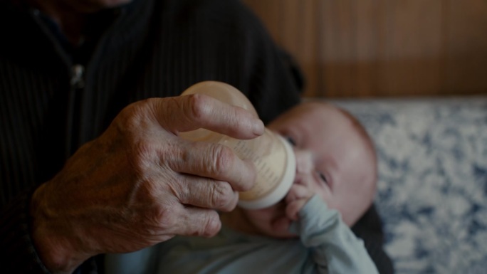 爷爷用手从家里的奶瓶里给小男孩喂奶的特写镜头