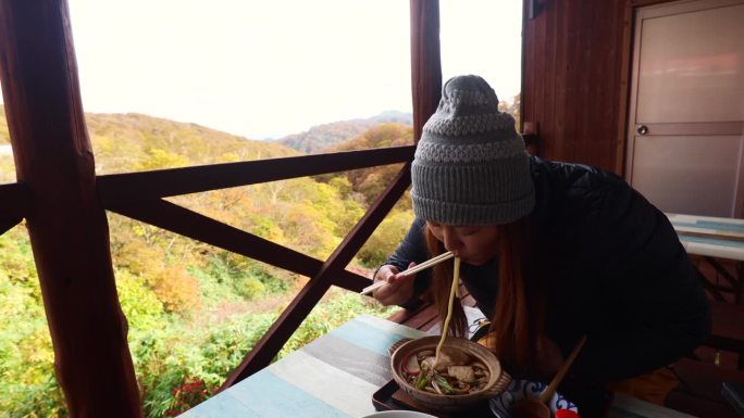 一名妇女在山间餐馆的阳台上吃乌冬面