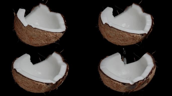 在黑色的背景上，用慢动作将椰子汁滴在半个椰子上旋转。