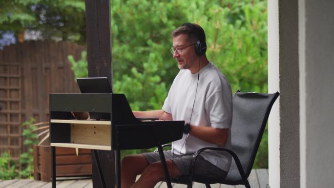 在户外工作。男人戴着耳机听音乐，盯着电脑屏幕学习