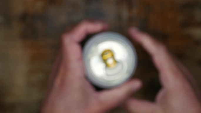 镜头:一个人打开一罐啤酒。有人从桌子上拿起一罐啤酒。拿着一罐啤酒的人。一个啤酒罐，俯视图，特写。饮酒