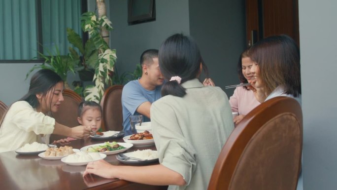 亚洲家庭吃中国菜，坐在后院的餐桌上玩得很开心。多代同堂的家庭一起享受消费。