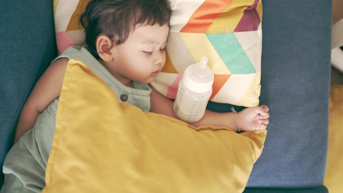 小女孩拿着奶瓶睡在客厅的沙发上。