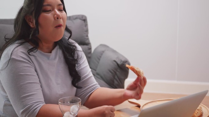 大码亚洲妇女享受披萨，而放松在家里的客厅。