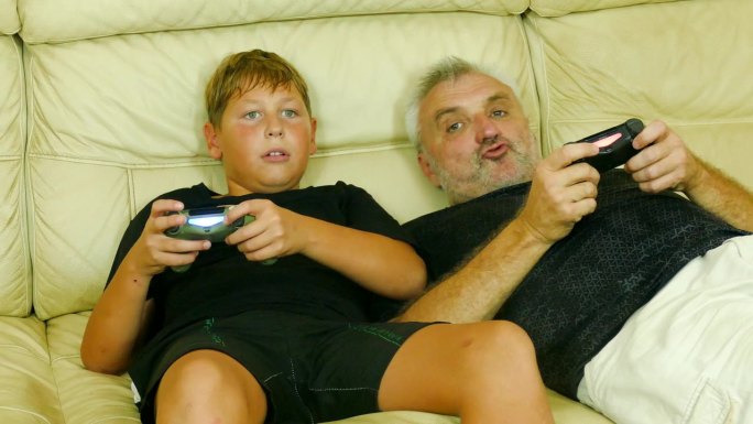 父子俩躺在沙发上玩电子游戏