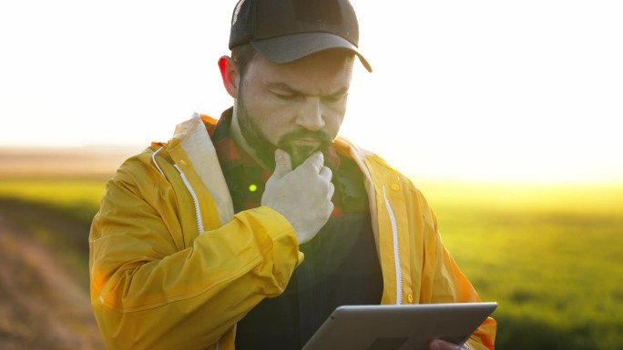 留胡子的帅哥拿着电子平板电脑在战场上。现代技术在农业种植活动中的应用。农学家在绿地上拿着药片。从事农
