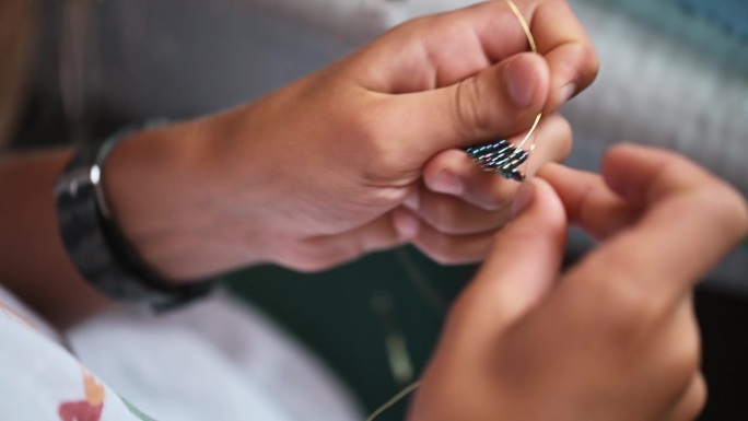 一个孩子正在勤奋地制作精致的珠饰，全神贯注地编织复杂的装饰品。双手热情地工作，创造出小小的杰作。