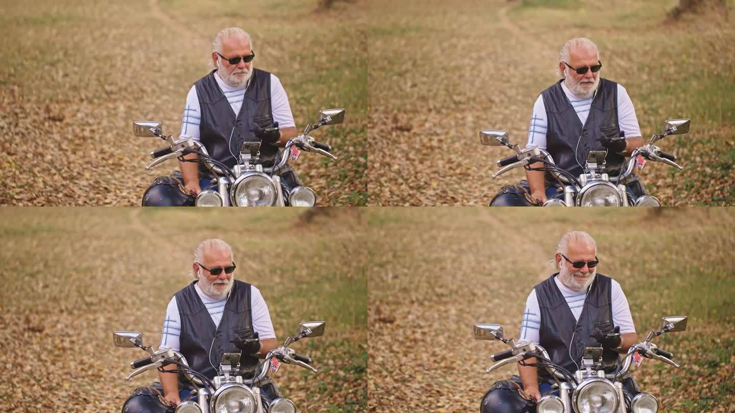 高级男性白人骑摩托车的人像坐在摩托车上，用耳机通过视频通话打电话