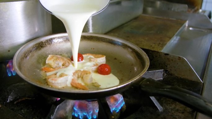 厨师在煤气灶上的锅里淋上浓奶油，还有虾、土豆和乳白色的面