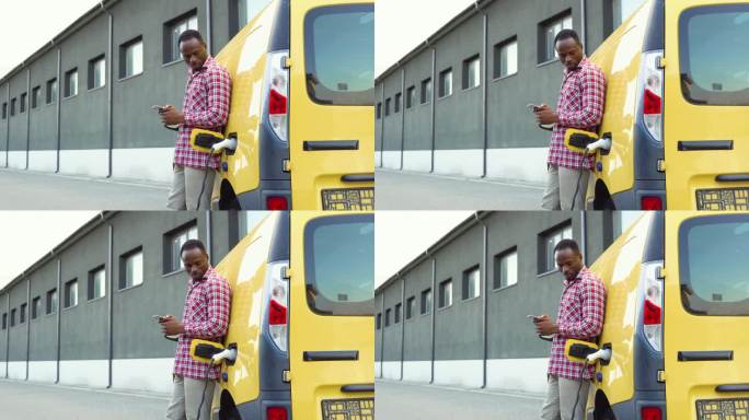 黑人男子手持智能手机在电动汽车充电站给卡车充电