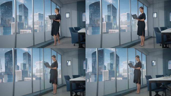 广角白人女商人站在摩天大楼的现代办公室里，使用笔记本电脑。成功的商业经理阅读邮件或检查任务。
