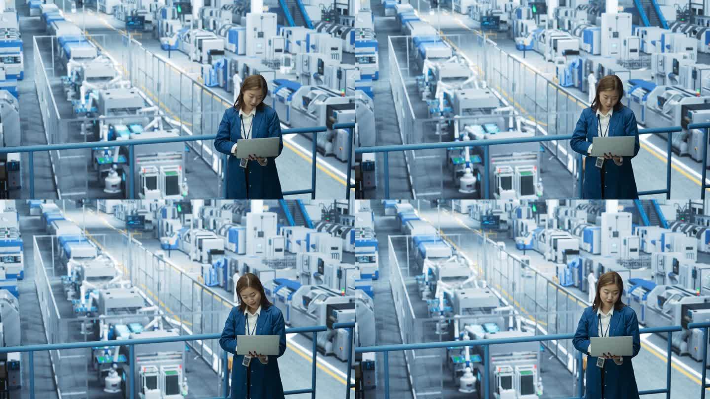 亚洲女工程师站在工厂设施里，用笔记本电脑工作，研究和开发现代自动化机械臂生产电子产品的技术