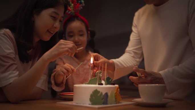 家庭回忆:当她的父母点燃她的生日蛋糕蜡烛时，可爱的小女孩兴奋的慢动作肖像。年轻的韩国夫妇庆祝他们的女