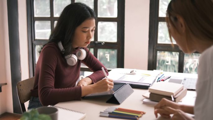 迷人的亚洲大学生使用笔记本电脑和平板电脑与一群朋友一起学习英语课堂，社交媒体和教育理念。