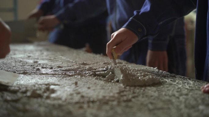 一群人以团队的形式工作，用镘刀在平面构件上涂抹水泥