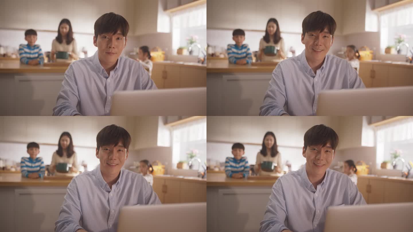 韩国年轻人在家里用笔记本电脑工作的肖像，看着镜头，微笑着，背景是他爱的家人。成功的商人得到亲人的支持