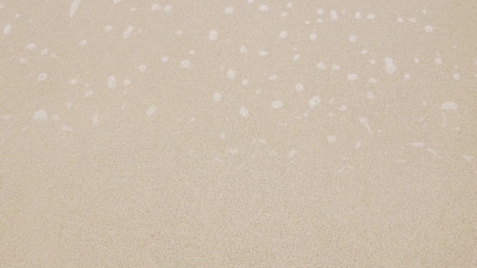 近距离观看海浪翻滚在细沙沙滩上，海浪在白色沙滩上拍打着美丽的泡沫，热带夏日假期的自然背景