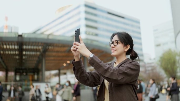 一位亚洲年轻女子独自站在日本的一个城市里。一个女人拍了一张照片，给朋友发了一条信息。