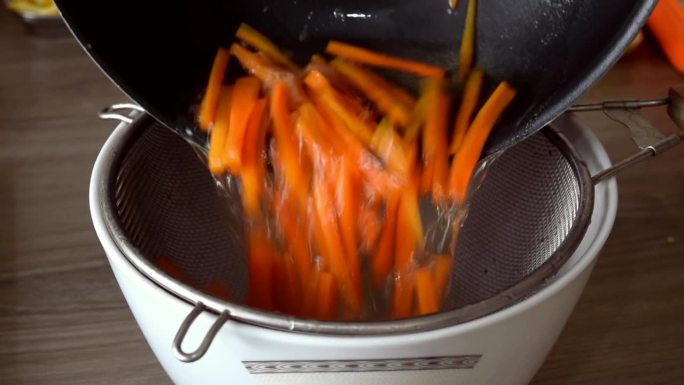 煮熟的胡萝卜被筛入白色的碗中，慢动作。平底锅，红胡萝卜，木桌。