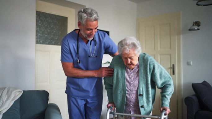 护工帮助家中的老年妇女从轮椅上站起来。