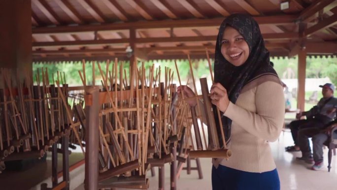 女穆斯林微笑着摇晃着angklung，这是一种来自爪哇的传统印尼乐器，由竹子制成。通过摇动来发出声音