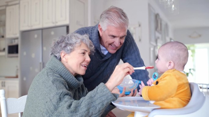 快乐的祖父母在家里一起给宝宝喂早餐，厨房里的爱和家庭纽带。微笑，食物和老人，女人和饥饿的孩子在公寓吃