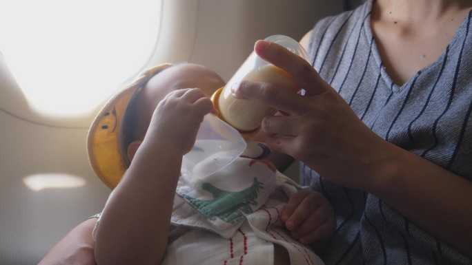家庭旅行瞬间:妈妈在飞机上用奶瓶喂儿子。