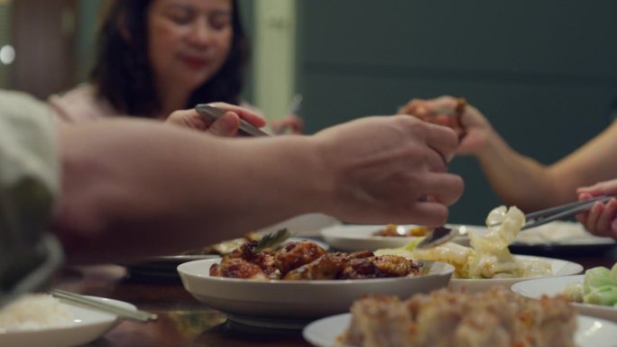 亚洲家庭吃中国菜的特写，晚上坐在家外后院的餐桌旁吃晚饭。多代同堂的家庭一起享受消费。