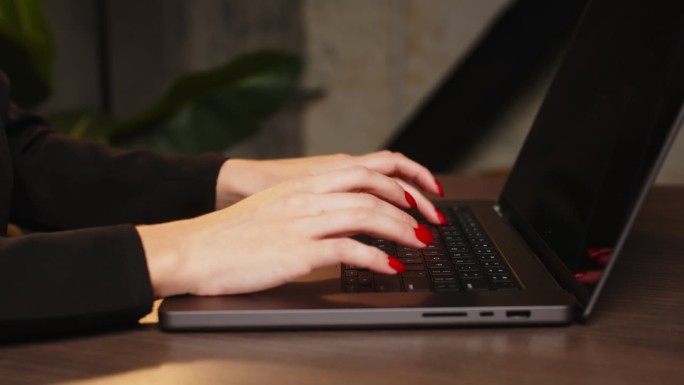 一个商业女性的女性手在笔记本电脑键盘上打字的特写，背景是深色的暖光灯。人与科技的理念。