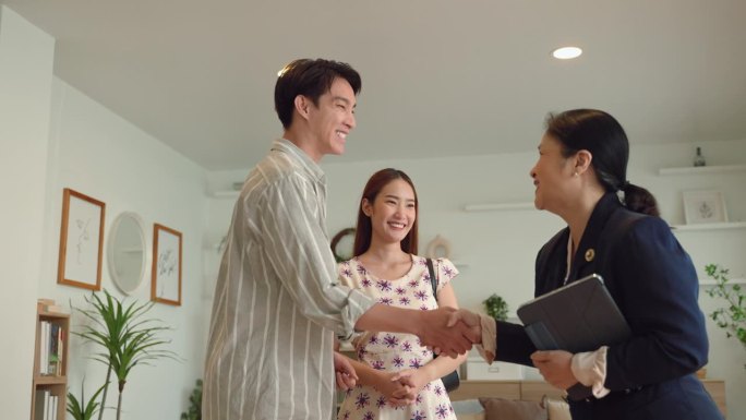 买房的年轻亚洲家庭从房地产经纪人那里拿到钥匙，拥抱在室内