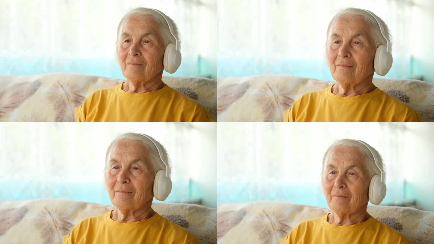 戴着耳机的白头发老妇人坐在家里的沙发上，听音乐、有声读物、讲座。概念音频治疗和声音治疗，学习。