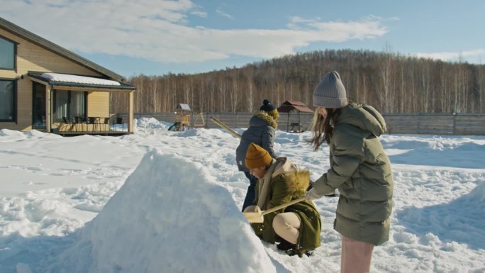 穿着保暖衣的不同少年在院子里建造雪堡