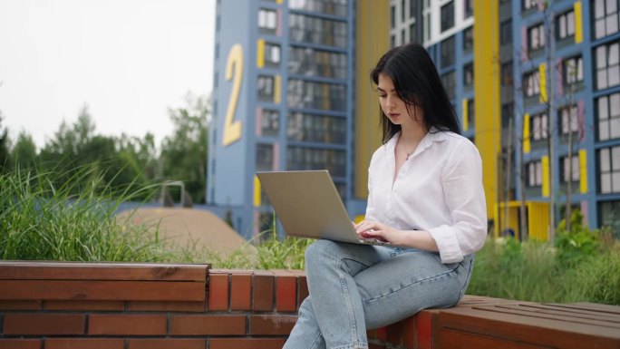女黑客在城市公园用笔记本电脑工作，忙碌的女商人用便携式电脑的肖像