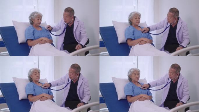 高级亚洲男医生坐在办公桌前，拿着听诊器，听着现代医院里正在康复的老年女病人的心跳、心肺检查。