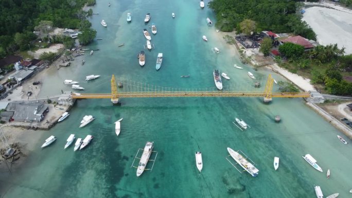 空中4K无人机镜头:踏板车穿过连接巴厘岛努沙莱姆邦根岛和努沙塞宁根岛的标志性和风景如画的黄桥;船散落