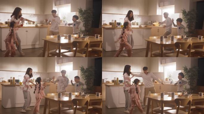 吃完营养早餐后，一家人在厨房里尽情跳舞。年轻的父母和他们可爱的孩子在早上听音乐玩得很开心