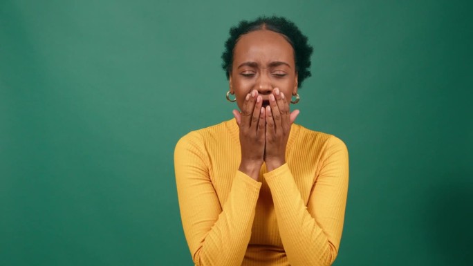 年轻的黑人妇女打着哈欠捂住嘴，绿色背景的演播室录像