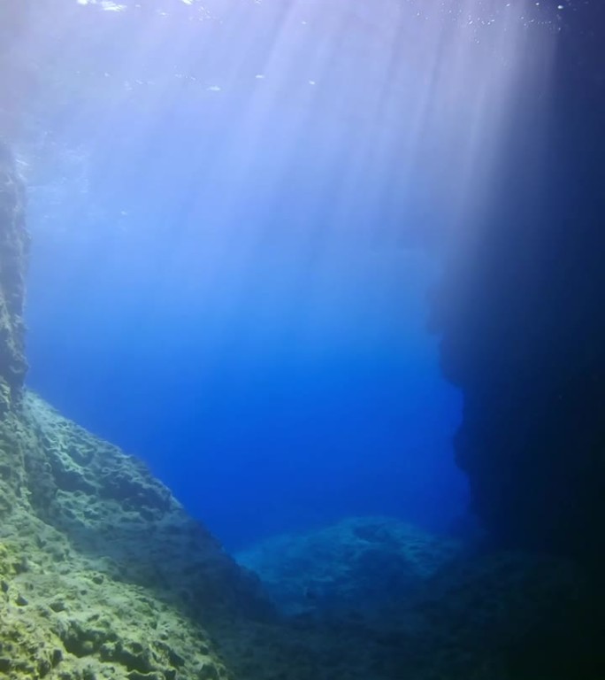 明亮的阳光穿透蓝色的海水，进入岩礁峡谷