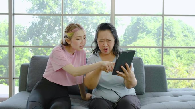 亚洲老年成熟女性视力不好，从平板电脑屏幕看不清楚，漂亮的女儿看到后过来帮忙看平板电脑上的信息，需要激