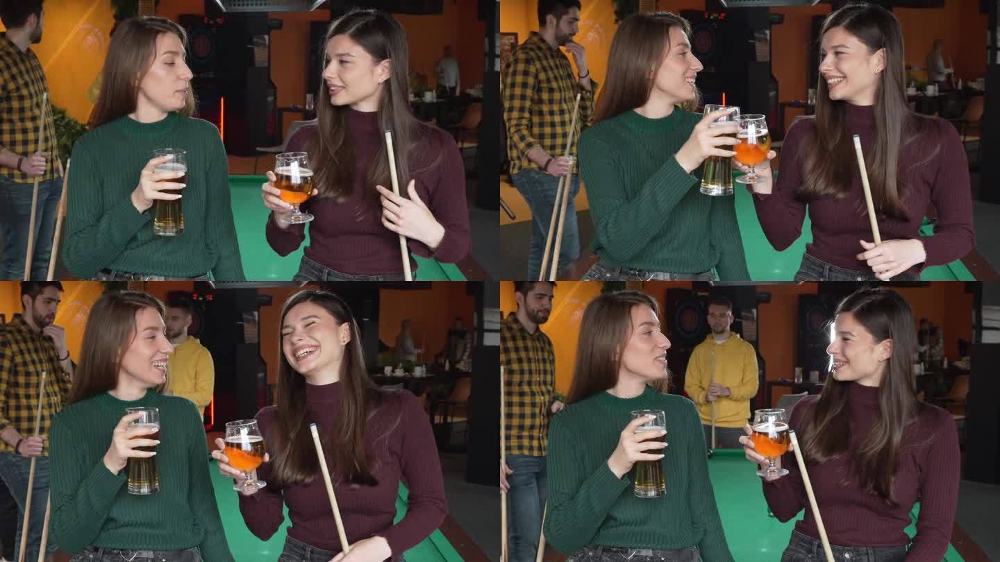 白人女性朋友一边喝啤酒，一边和男性朋友在酒吧打台球桌