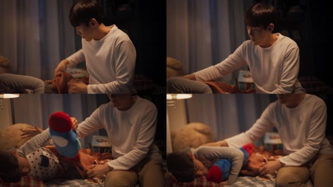 韩国年轻父亲照顾他可爱的儿子，晚上把他放在家里的床上睡觉。男父母给小男孩盖上毯子，确保他晚上温暖舒适