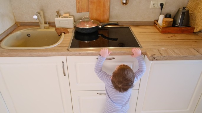 婴儿爬上家庭厨房的热电炉。小孩子用手触摸炉子的表面，有被烧伤的危险。两岁左右(一岁九个月)
