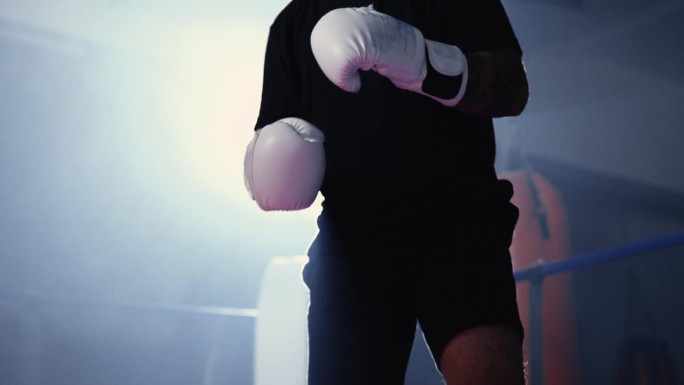 拳击场内的拳击手戴着拳击手套，在戏剧性的灯光下待命