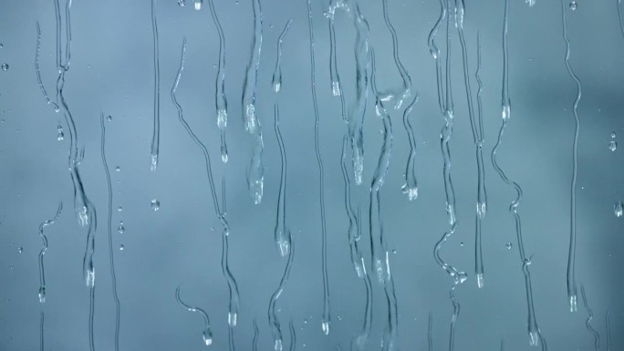 雨滴顺着玻璃流下来。窗外下着大雨，天气越来越糟。慢镜头，蓝色背景