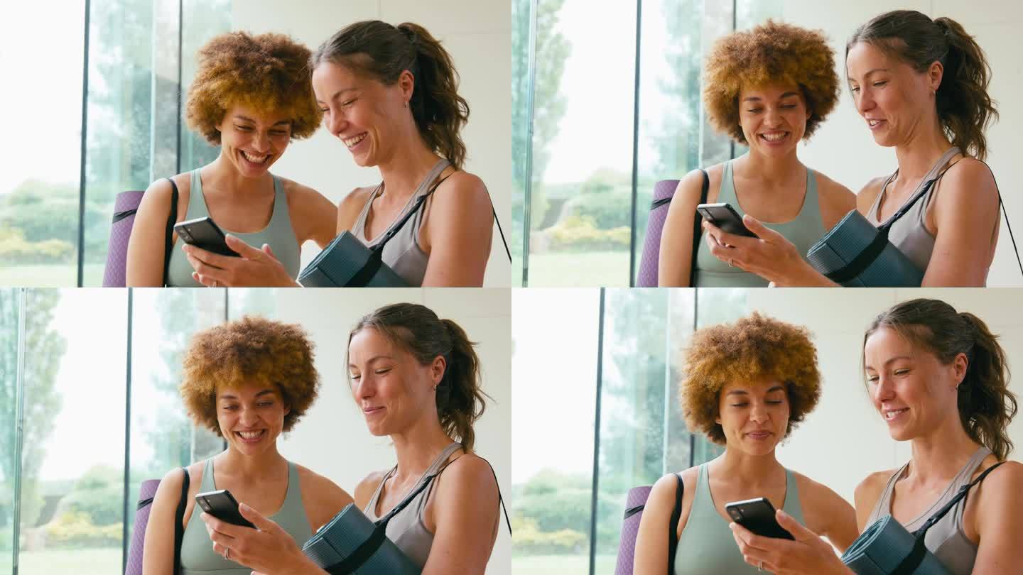两个女性朋友穿着运动服在健身房或瑜伽馆看手机