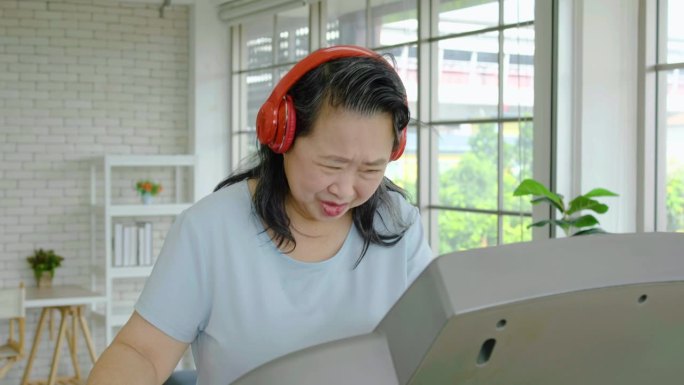 年长的亚洲女性祖母戴着耳机，用智能手机给朋友或家人打视频电话，展示她在家锻炼时取得的成就和结果