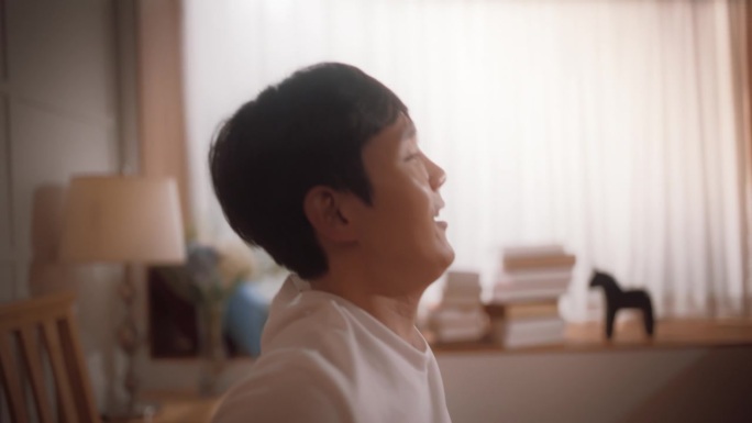 韩国帅哥被阳光从窗户照进来唤醒的跟踪镜头。快乐的亚洲男性在家里迎接新的阳光灿烂的一天，舒展身体，准备