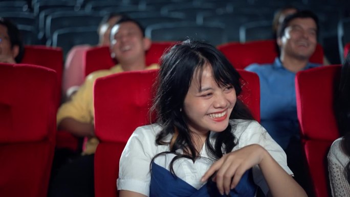 年轻的亚洲妇女笑着享受在电影院看电影。